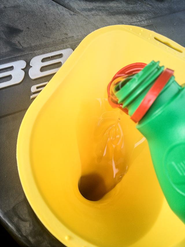Verse motorolie loopt uit een groene fles in een gele trechter