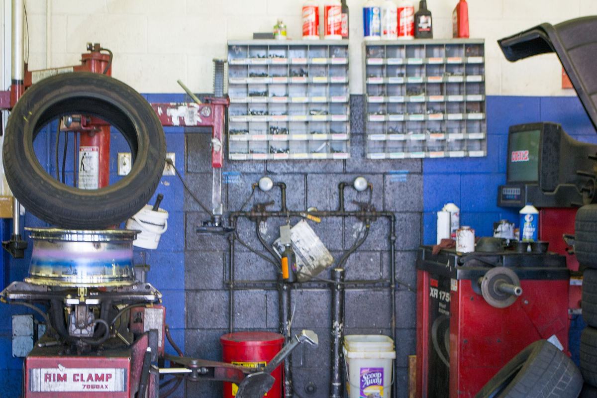 Werkplaats met een bandenmontagemachine, een balanceertoestel en kasten vol kleine onderdelen tegen een blauwe muur