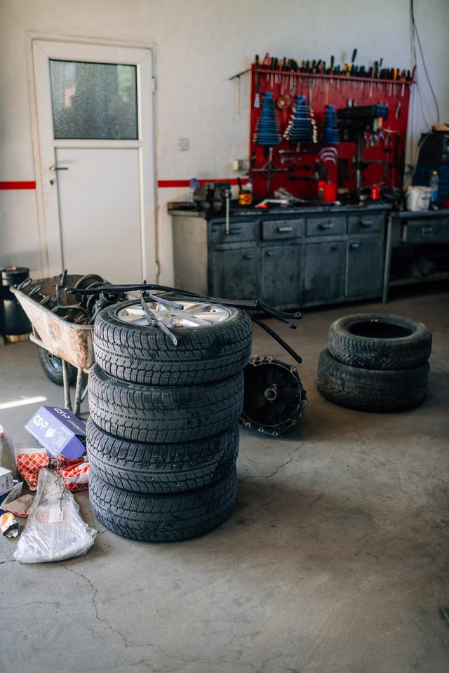 Een stapel autobanden op de vloer van een werkplaats, met een werkbank en gereedschap op de achtergrond